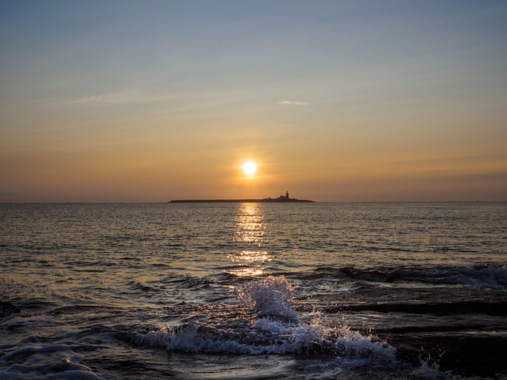 A splash of water from a wavelet, with the sun rising behind Coquet Island.