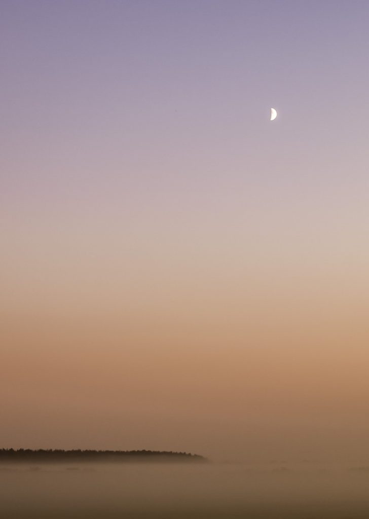 Moon over misty fields at sunset