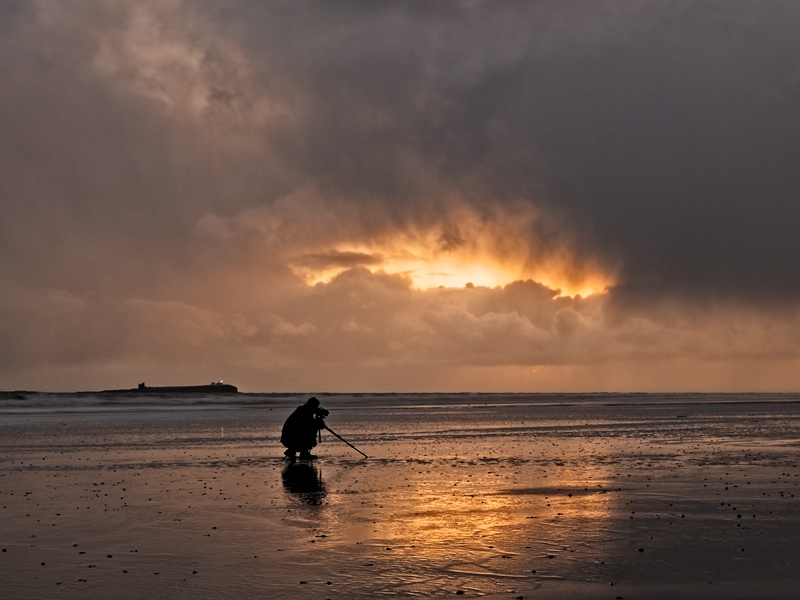 Reliable ancillary equipment like a tripod is essential. Man on beach shooting the sunrise.
