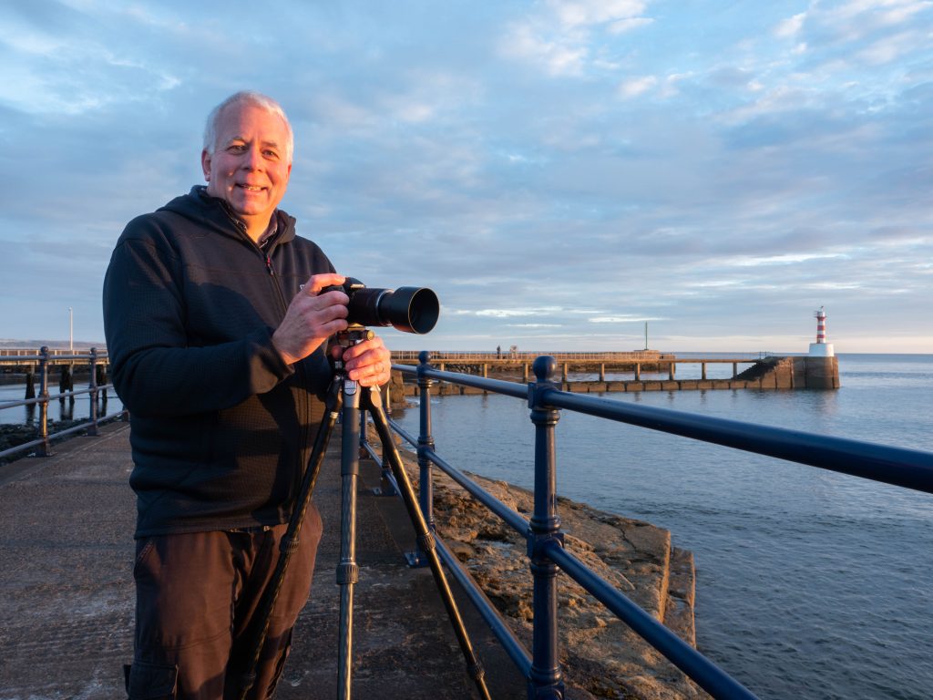 Ivor Rackham, photographer, stands with an OM-1 Mark II and the OM System OM-1 Mark II on a Benro tripod