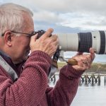 Ivor Rackham, photographer, stands with an OM-1 Mark II and the OM System 150-400 mm F4 PRO lens