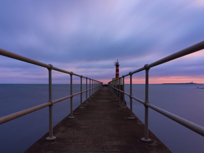 A long exposure of Amble Pier before dawn. The sea is smooth and the clouds show signs of movement.