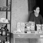 A woman street vendor stands behind her outdoor store selling groceries. She is staring at something to the right, out of the frame