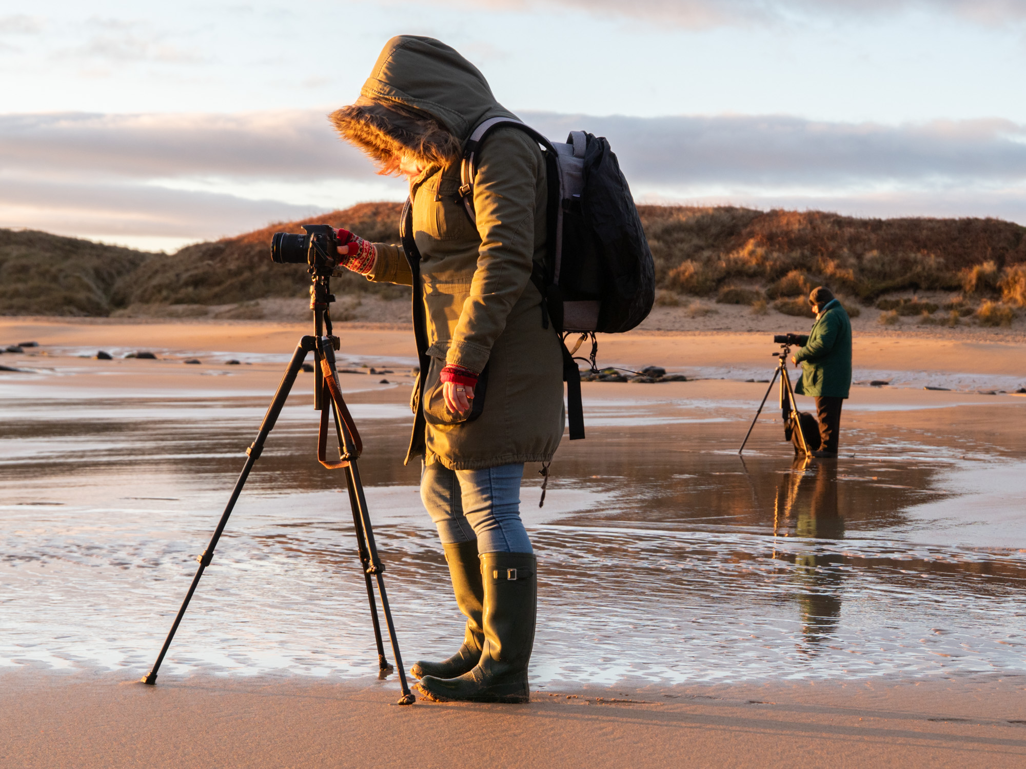 Two people on a photography workshop with Ivor Rackham take photos on the beach at sunrise.