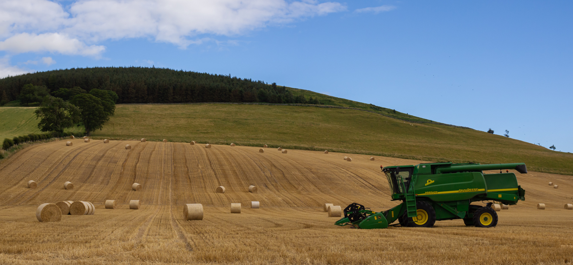 a panoramic photo of farmland and hills with a John Deere combine harvester in the field