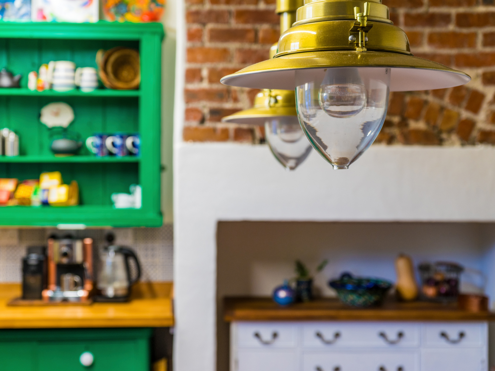 An interior view of a farmhouse/cottage-style kitchen with two brass light hangings.