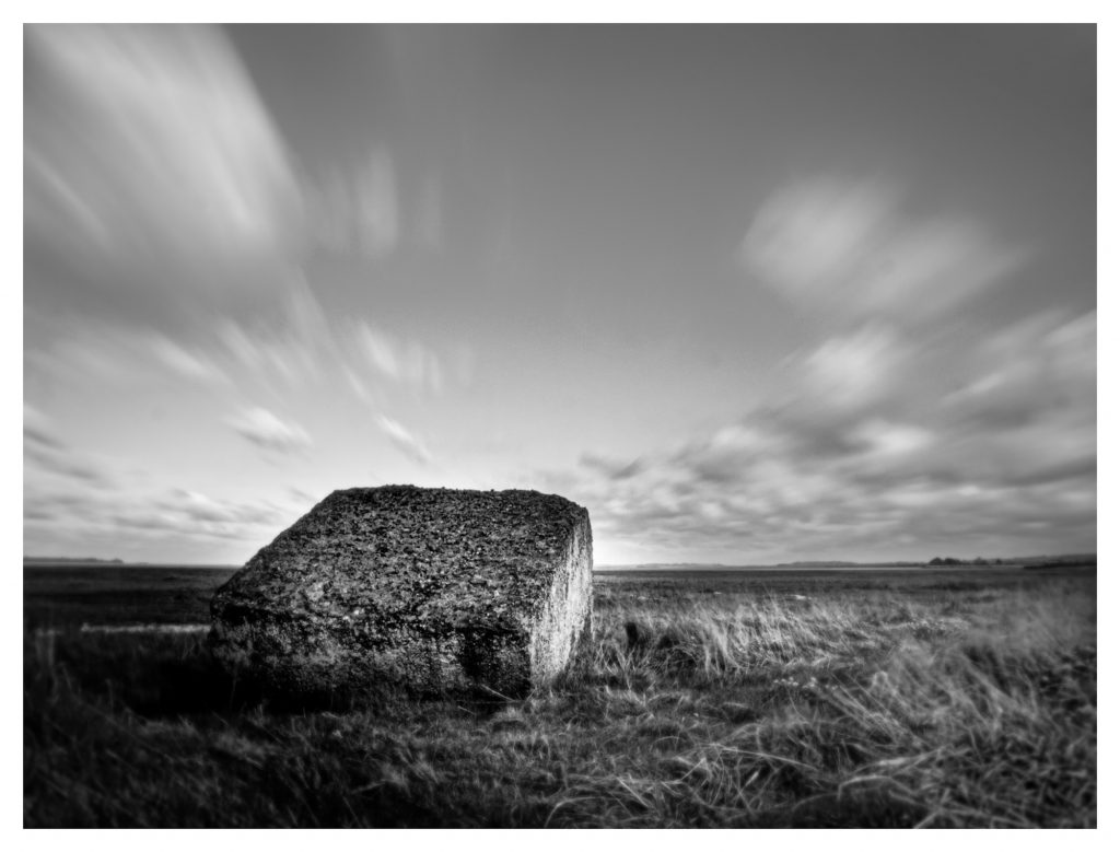 Fast moving clouds drift over a World War II coastal defence block. Black and white long exposure image.