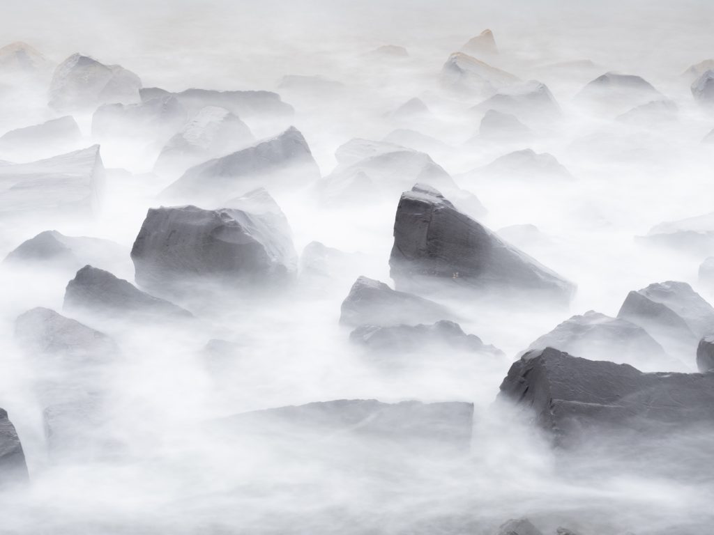 A long exposure photo of rocks with the water looking like clouds floating around them.