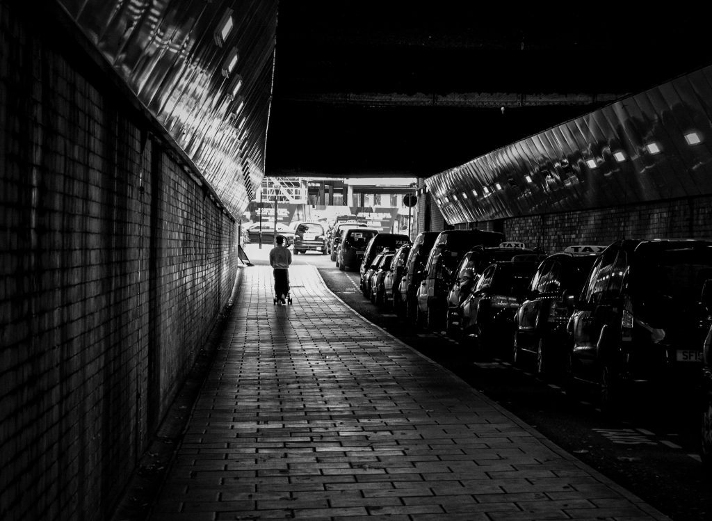 Photographed on a Street Photography class in Newcastle-upon-Tyne, a black and white image of a tunnel. On the right is a row of taxis, a woman walking away from the camera is in the right,